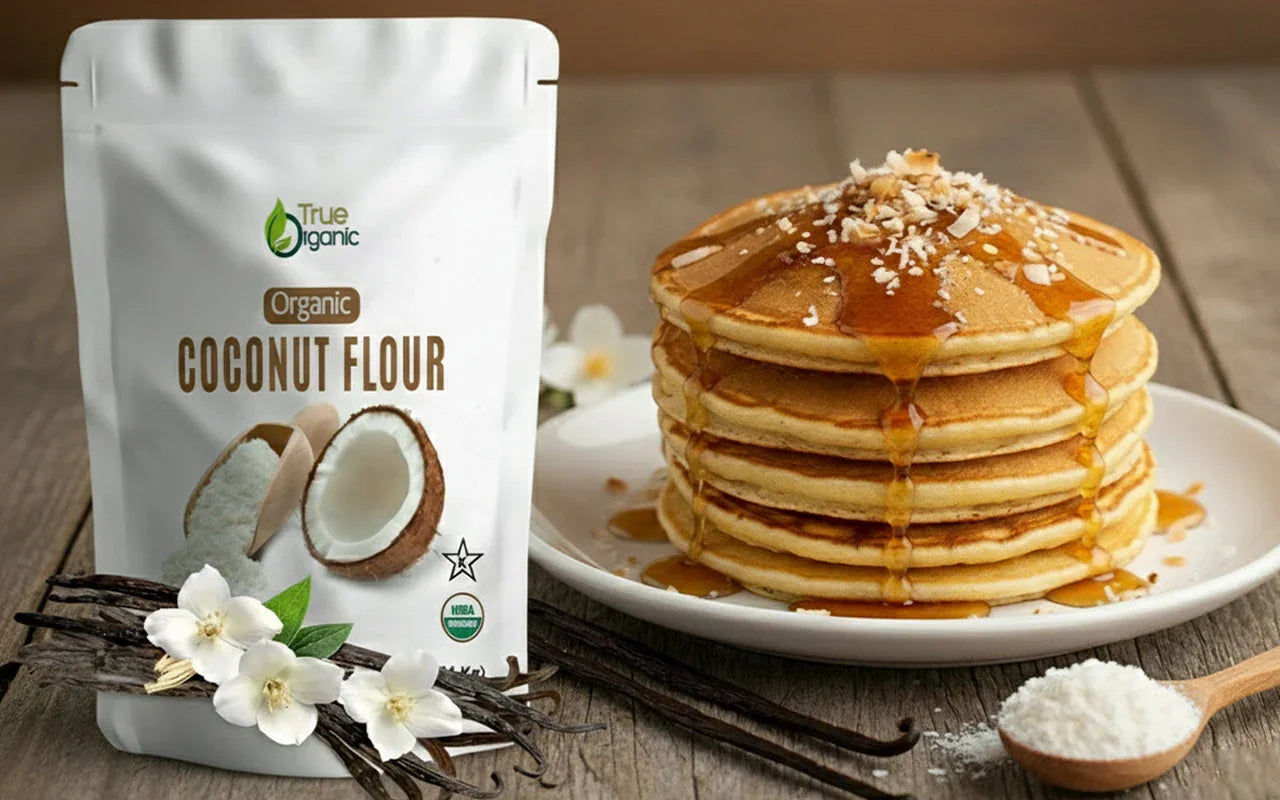 Stack of pancakes drizzled with syrup next to organic coconut flour package and vanilla beans on wooden table