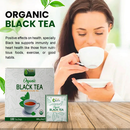 Woman enjoying organic black tea with True Organic premium Ceylon tea boxes on wooden table