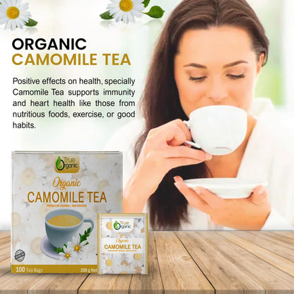 Woman drinking organic chamomile tea with True Organic tea packaging on wooden table